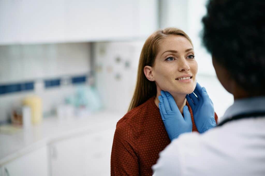 Smiling woman having thyroid exam at doctor's office.