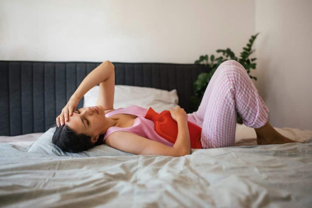 Woman at home suffering from menstrual pain. Menstrual cramps, woman warming lower abdomen with a
