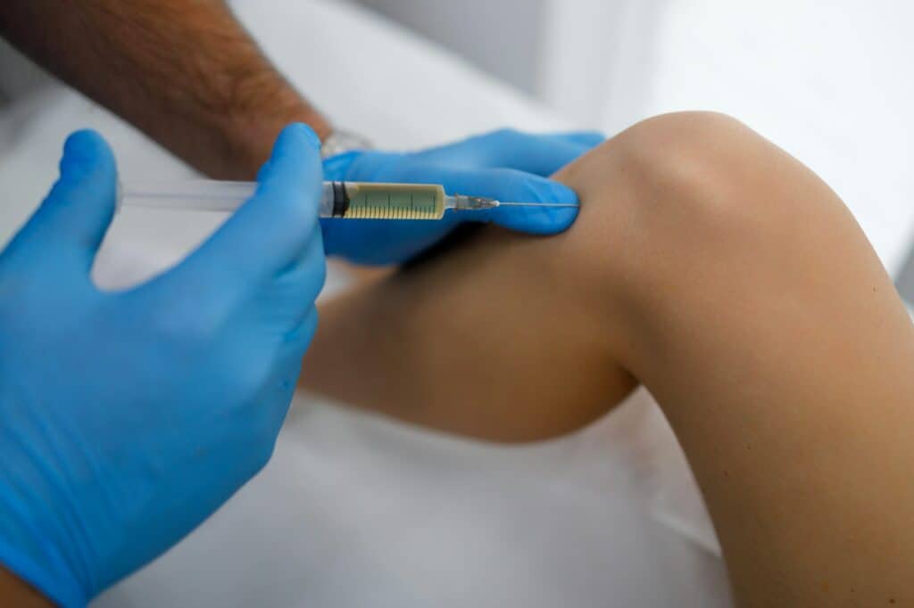Close up view of orthopedic doctor hands make plasma injection in knee